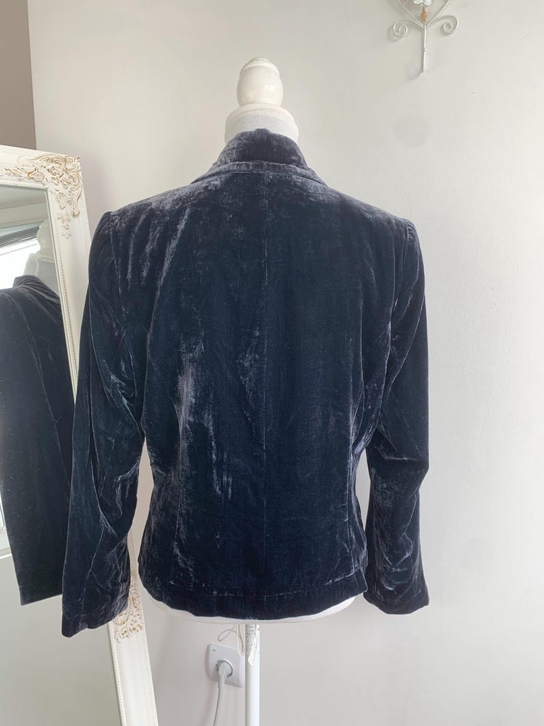 May include: A dark navy blue velvet blazer displayed on a mannequin. The blazer has long sleeves and a classic collar. The fabric has a soft, textured appearance. The blazer is a sophisticated piece of apparel.