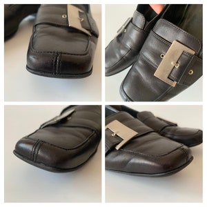 K&ouml;nnte beinhalten: Schwarze Leder-Slipper mit einer silbernen Schnalle. Die Slipper haben eine quadratische Spitze und einen niedrigen Absatz.