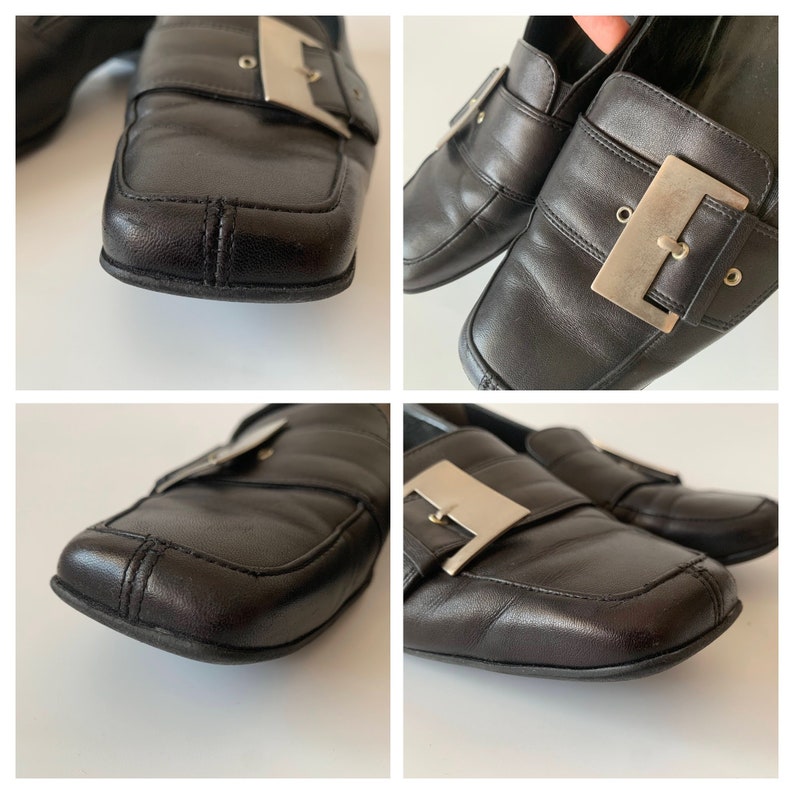 K&ouml;nnte beinhalten: Schwarze Leder-Slipper mit einer silbernen Schnalle. Die Slipper haben eine quadratische Spitze und einen niedrigen Absatz.