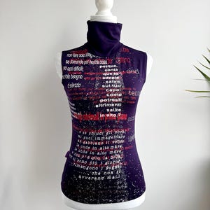 May include: A sleeveless, dark purple top with a high turtleneck collar. The top is covered in white and red text. The text appears to be in a foreign language. The top is displayed on a white mannequin.