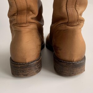 May include: A pair of brown leather boots with a slouchy shaft and a dark brown sole.