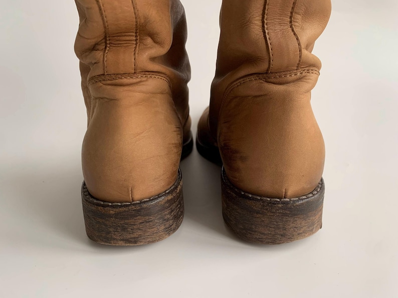 May include: A pair of brown leather boots with a slouchy shaft and a dark brown sole.