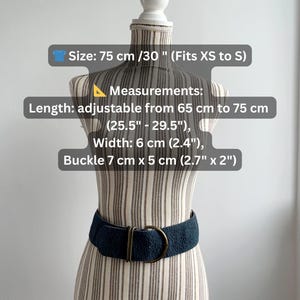 May include: A navy blue belt with a textured surface and a gold-coloured buckle. The belt is displayed on a mannequin. The belt is adjustable from 65 cm to 75 cm and is 6 cm wide. The buckle is 7 cm x 5 cm.