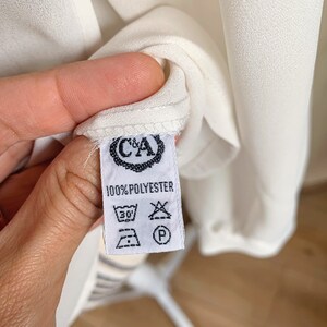 Puede incluir: Etiqueta de cuidado blanca con texto negro que dice "100% POLYESTER" e incluye instrucciones de lavado. La etiqueta tiene un logotipo con las letras "C&A" en un c&iacute;rculo.