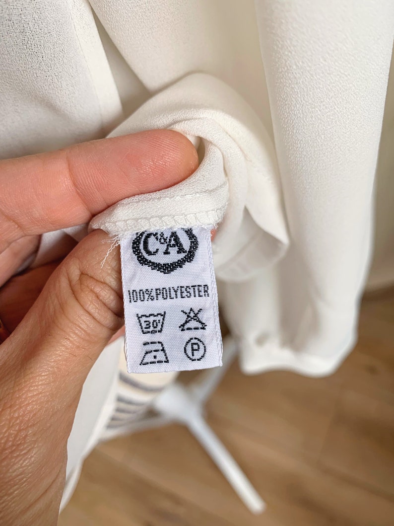 Puede incluir: Etiqueta de cuidado blanca con texto negro que dice "100% POLYESTER" e incluye instrucciones de lavado. La etiqueta tiene un logotipo con las letras "C&A" en un c&iacute;rculo.