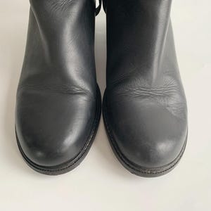 May include: A pair of black leather ankle boots with a rounded toe design and a smooth, matte finish. The boots feature a low heel and a simple, clean construction with visible stitching along the sole edge, showcasing a classic and functional footwear style.