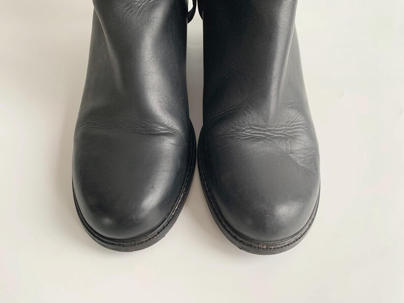 May include: A pair of black leather ankle boots with a rounded toe design and a smooth, matte finish. The boots feature a low heel and a simple, clean construction with visible stitching along the sole edge, showcasing a classic and functional footwear style.