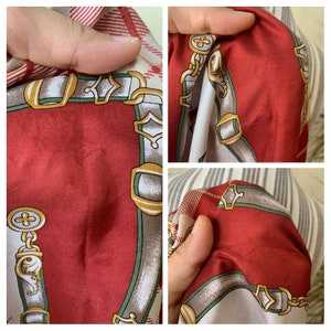 May include: Red silk scarf with a white and green pattern of chains and buckles. The scarf has a subtle plaid pattern in the background.