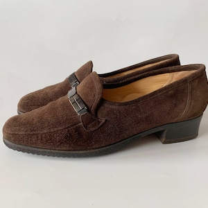 May include: Brown suede heeled loafers with a silver buckle detail.