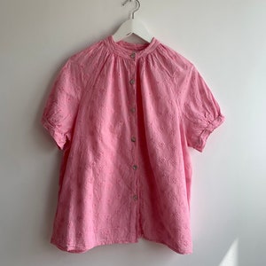 Puede incluir: Una camisa rosa de manga corta con botones y estampado floral.