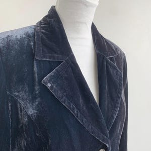 May include: A dark blue velvet blazer with a notched lapel and a single button closure. The blazer has a classic design and a soft, textured appearance. The button is silver with a decorative design.