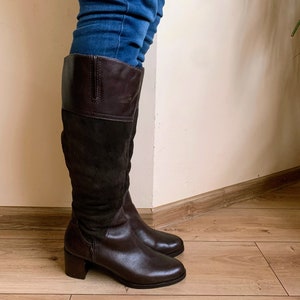 May include: Brown leather knee-high boots with a block heel. The boots have a suede panel on the back of the shaft.