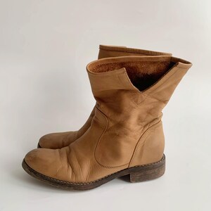 May include: Tan leather ankle boots with a slouchy fit and a low heel.