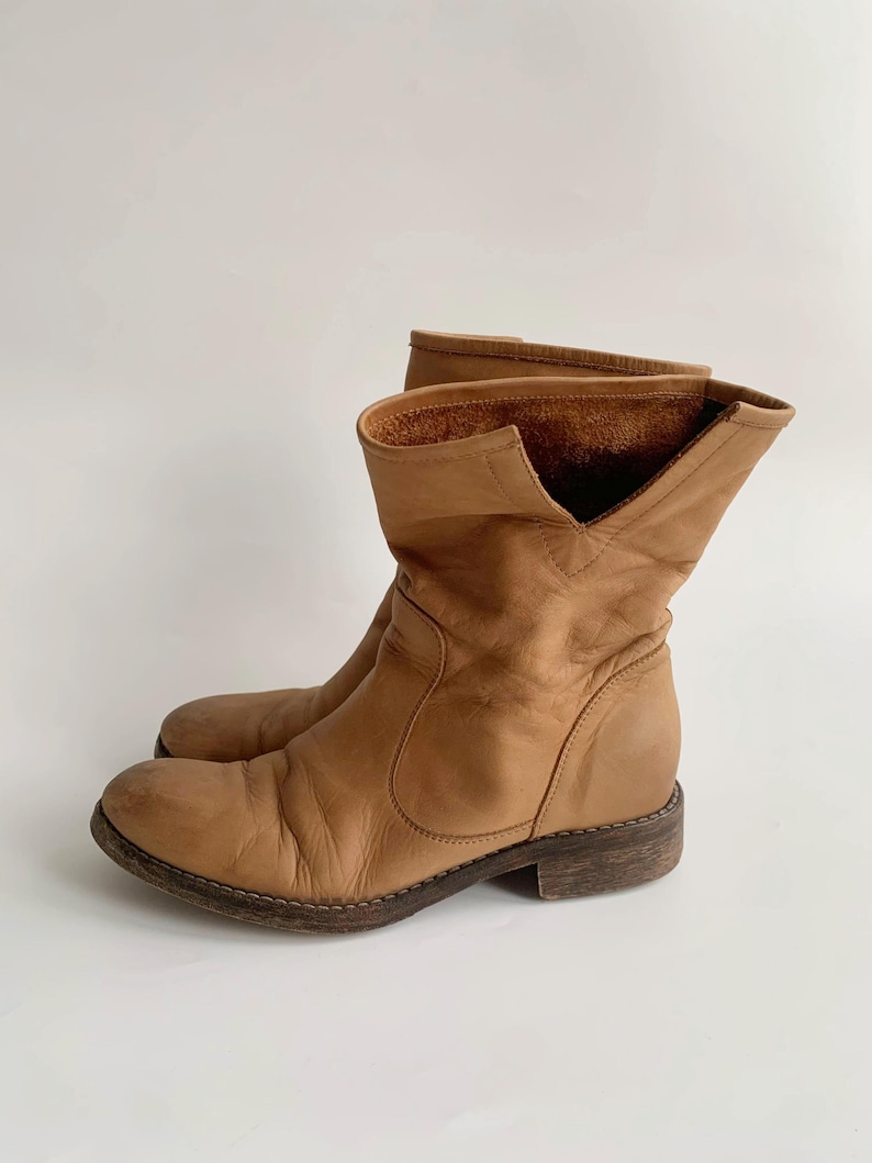 May include: Tan leather ankle boots with a slouchy fit and a low heel.