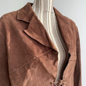 May include: A brown suede jacket with a long, flowing style. The jacket has a tie closure at the front and a collar.