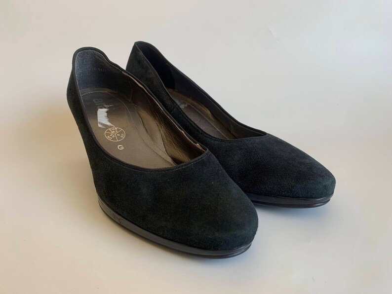 May include: A pair of black suede heeled shoes. The shoes have a pointed toe and a low heel.