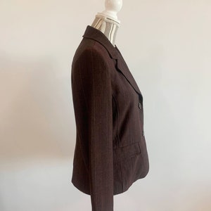 May include: A brown blazer with thin white pinstripes. The blazer has a double breasted closure with two buttons and a single pocket on the left side.