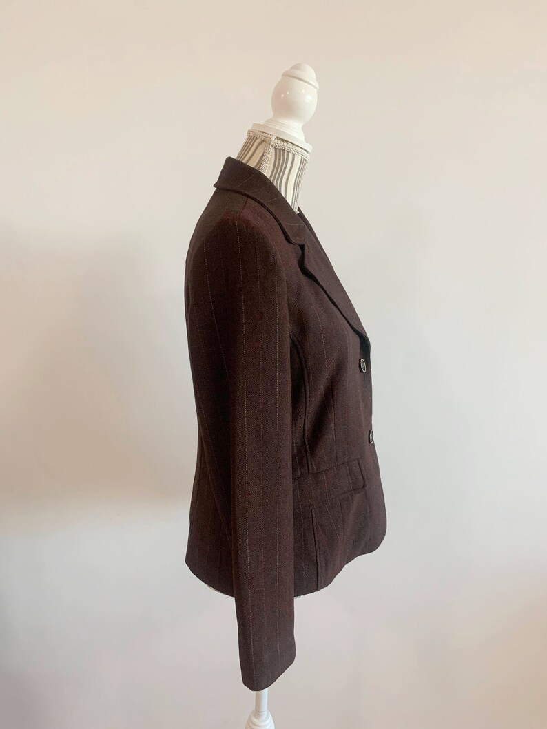May include: A brown blazer with thin white pinstripes. The blazer has a double breasted closure with two buttons and a single pocket on the left side.
