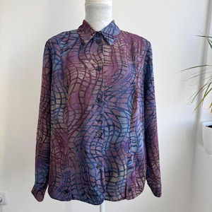 May include: A long-sleeved button-down shirt featuring a dark purple and blue abstract grid pattern. The garment has a standard collar, a full-length front button placket with dark buttons, and buttoned cuffs, displayed on a white mannequin.