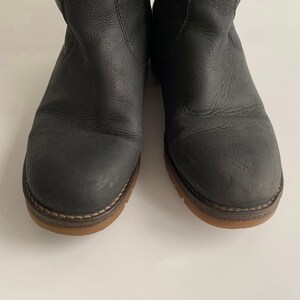 May include: A pair of dark grey leather ankle boots featuring a rounded toe, visible stitching along the welt, and a flat, light brown rubber sole. The boots have a textured leather upper with subtle creasing and a simple, clean design.