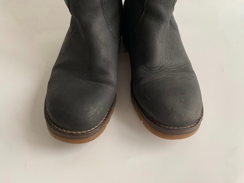 May include: A pair of dark grey leather ankle boots featuring a rounded toe, visible stitching along the welt, and a flat, light brown rubber sole. The boots have a textured leather upper with subtle creasing and a simple, clean design.