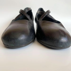 Pu&ograve; includere: Un paio di ballerine in pelle nera con un design a cinturino incrociato.