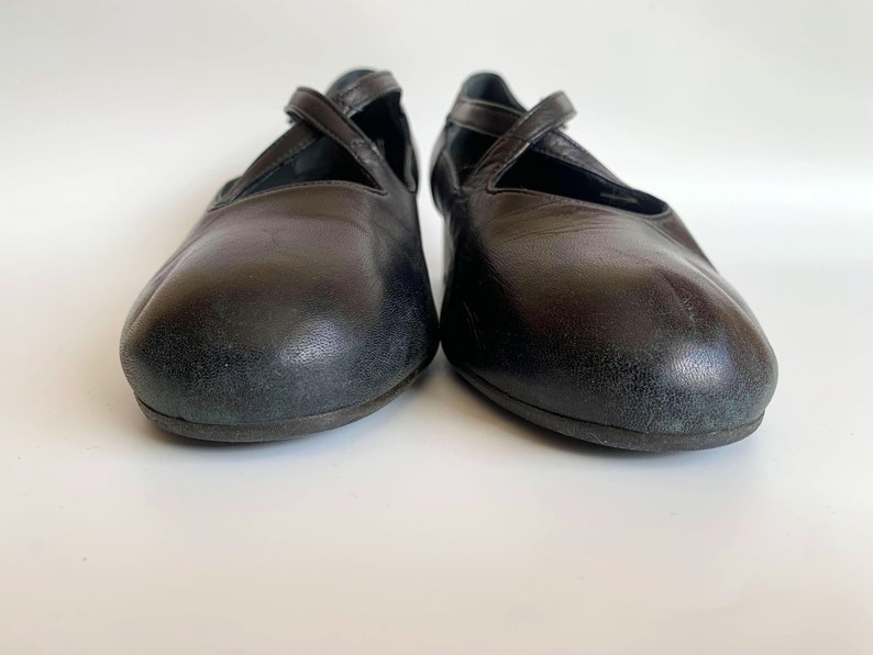 Pu&ograve; includere: Un paio di ballerine in pelle nera con un design a cinturino incrociato.