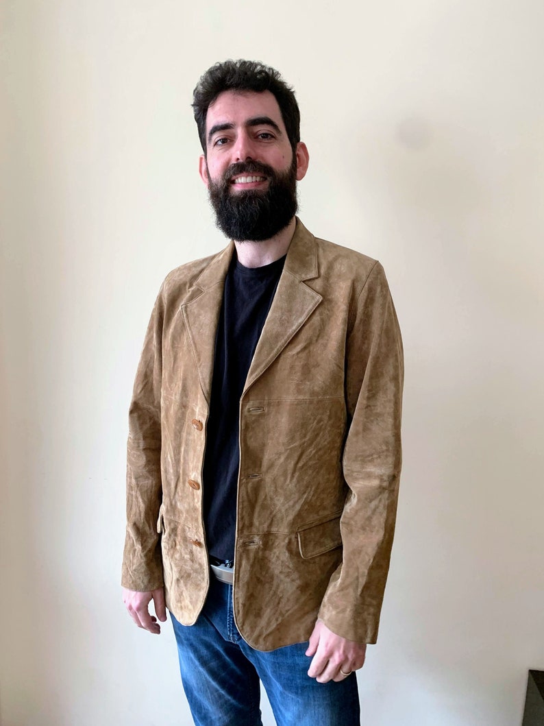 May include: A brown suede jacket with a button closure and two pockets. The jacket has a slightly textured surface.