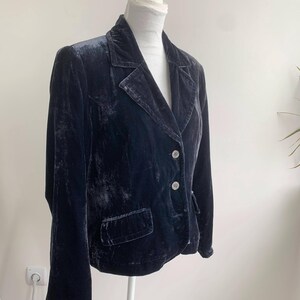May include: A dark navy blue velvet blazer with a classic notched lapel collar and two front pockets. The blazer has two decorative buttons and is displayed on a mannequin.