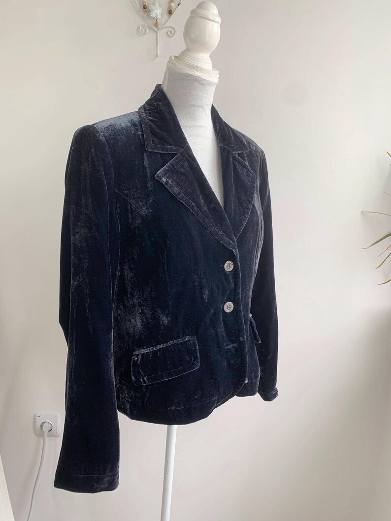 May include: A dark navy blue velvet blazer with a classic notched lapel collar and two front pockets. The blazer has two decorative buttons and is displayed on a mannequin.