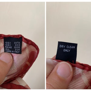 May include: A red and white silk scarf with a label that reads "100% seta 100% soie reine seide all silk made in Italy" and a separate label that reads "dry clean only".