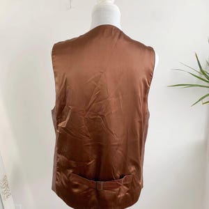May include: Back view of a brown vest on a mannequin. The vest has a satin-like sheen and a small belt detail at the waist. The vest is displayed against a plain white background.
