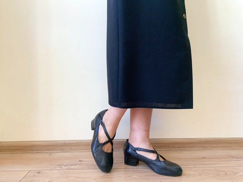 Pu&ograve; includere: Un paio di scarpe in pelle nera con un design a cinturino incrociato e un tacco basso a blocco.