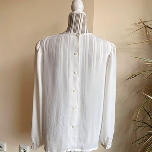 Puede incluir: Una blusa blanca transparente de manga larga con botones en la espalda.