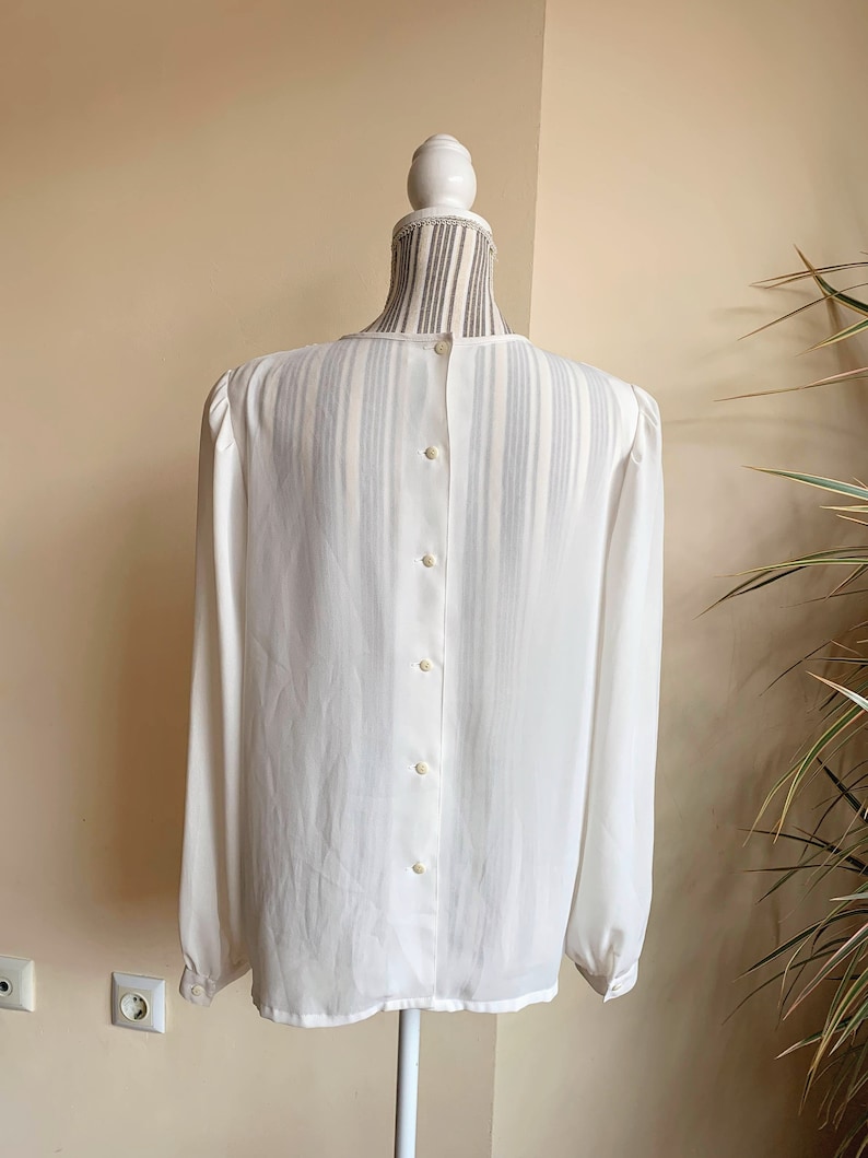 Puede incluir: Una blusa blanca transparente de manga larga con botones en la espalda.