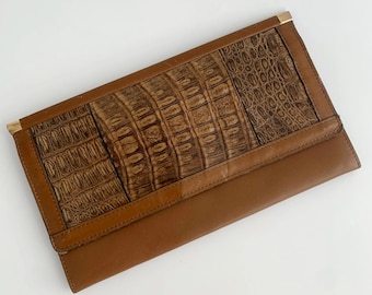 May include: A brown leather clutch with a crocodile embossed pattern. The clutch has a gold metal closure.