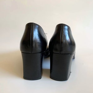 May include: A pair of black leather shoes with block heels. The shoes have a classic design with a rounded toe and a smooth, glossy finish. The heels are approximately 3 inches high.