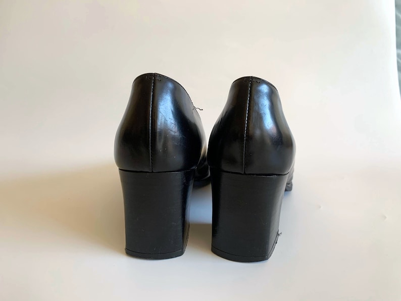 May include: A pair of black leather shoes with block heels. The shoes have a classic design with a rounded toe and a smooth, glossy finish. The heels are approximately 3 inches high.
