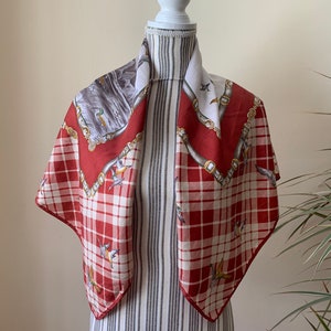 May include: A red and white plaid silk scarf with a gold chain and bird design. The scarf is displayed on a white mannequin.