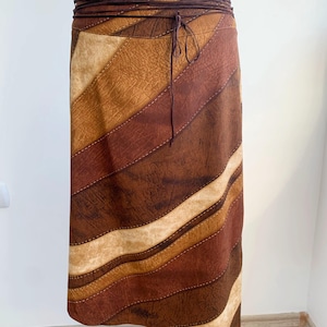 May include: A brown suede skirt with a geometric pattern of tan and brown stripes. The skirt has a brown leather tie belt.