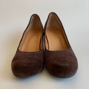 May include: A pair of brown suede heeled shoes. The shoes have a rounded toe and a low heel.