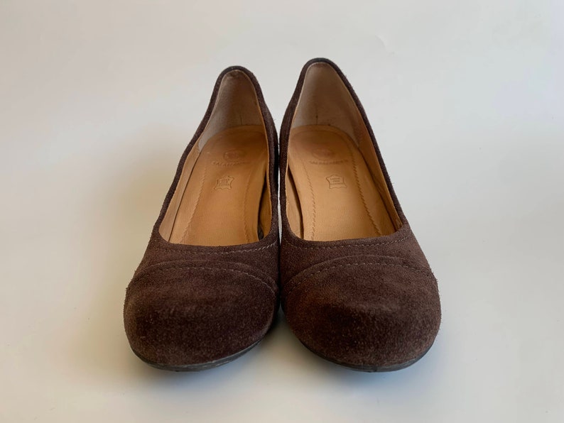 May include: A pair of brown suede heeled shoes. The shoes have a rounded toe and a low heel.