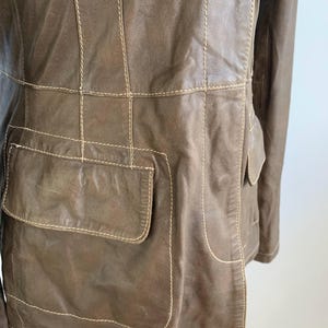 Op de afbeelding: Bruine leren jas met zichtbare stiksels en twee voorzakken. De jas heeft een klassiek ontwerp met een getailleerde pasvorm. De stiksels zijn lichter van kleur dan de jas, wat een contrast cre&euml;ert. De jas is van gemiddeld gewicht.