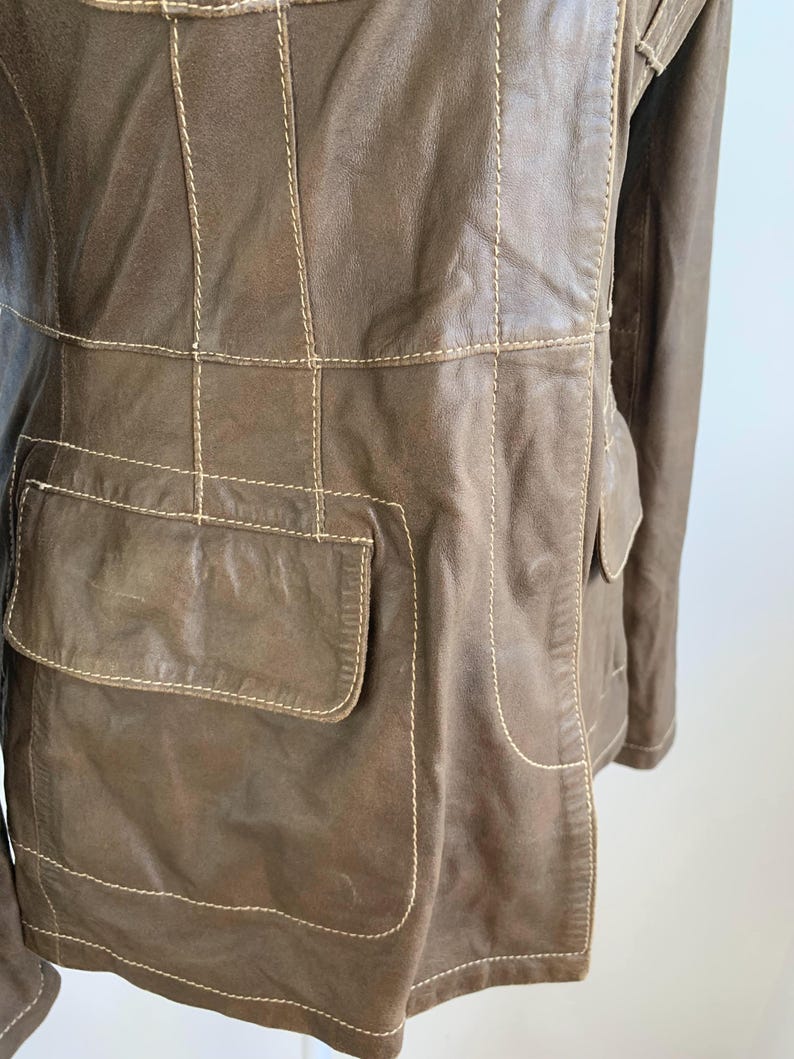 Op de afbeelding: Bruine leren jas met zichtbare stiksels en twee voorzakken. De jas heeft een klassiek ontwerp met een getailleerde pasvorm. De stiksels zijn lichter van kleur dan de jas, wat een contrast cre&euml;ert. De jas is van gemiddeld gewicht.