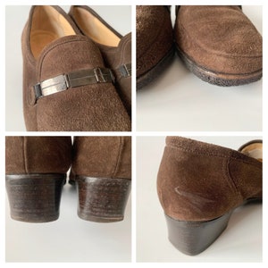 May include: Brown suede heeled loafers with a silver buckle detail. The shoes have a low block heel and a pointed toe.