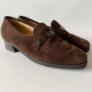 May include: Brown suede heeled loafers with a black buckle detail.