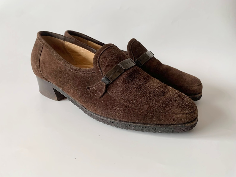 May include: Brown suede heeled loafers with a black buckle detail.