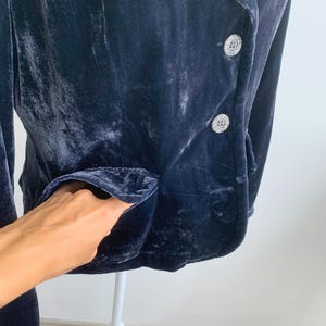May include: A navy blue velvet blazer with two decorative buttons and two pockets. The blazer is displayed on a white mannequin. The fabric has a soft, textured appearance.