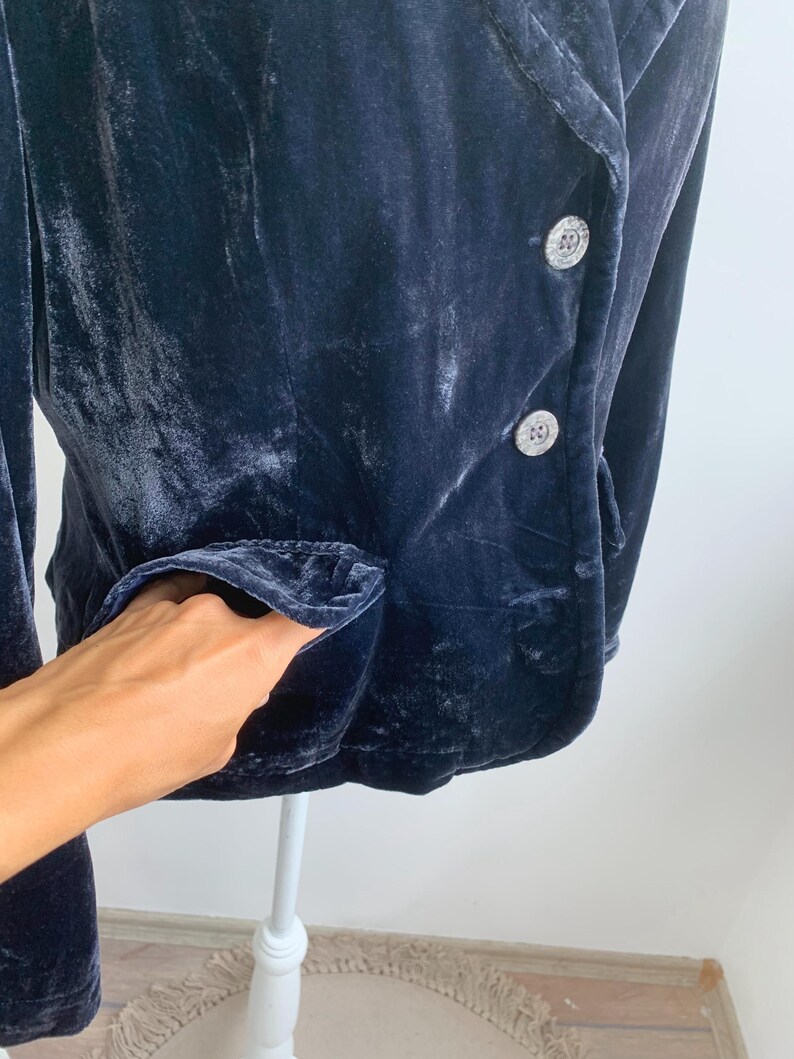 May include: A navy blue velvet blazer with two decorative buttons and two pockets. The blazer is displayed on a white mannequin. The fabric has a soft, textured appearance.