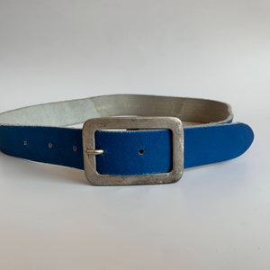 Pu&ograve; includere: Una cintura in pelle blu con una fibbia argentata.